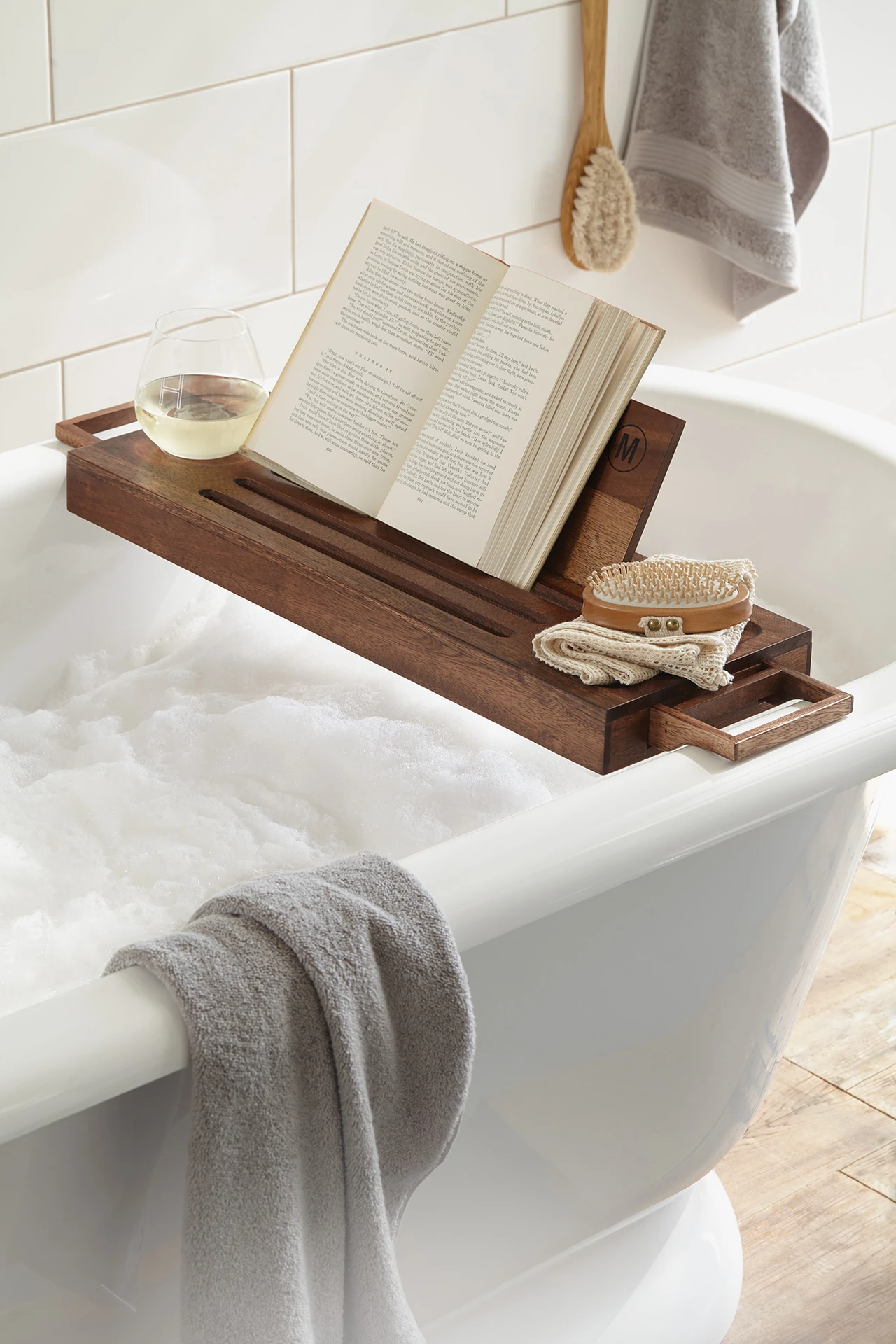 Wooden bath tray with candle and book across a bathtub