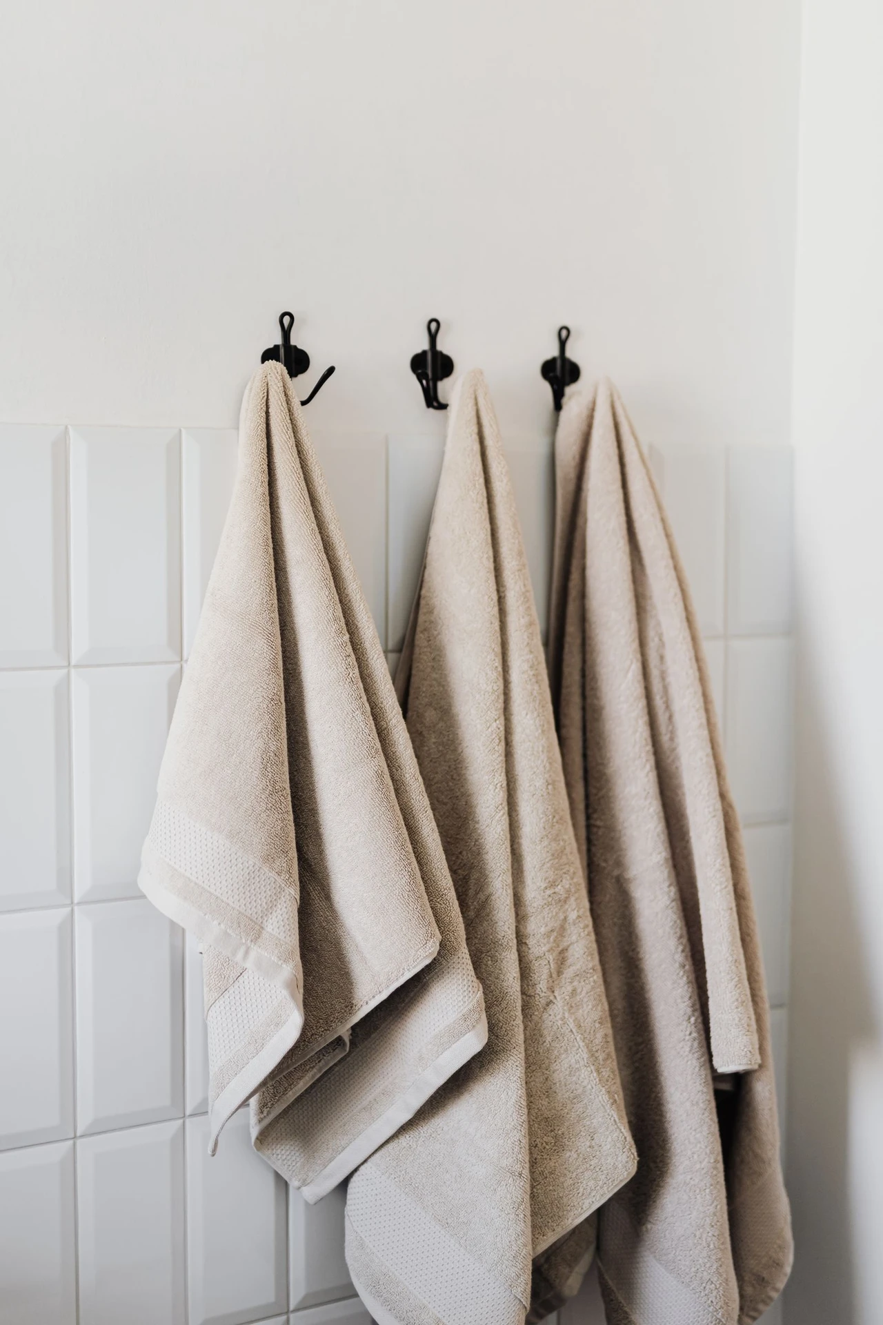 Matte black wall hooks holding towels in a modern bathroom