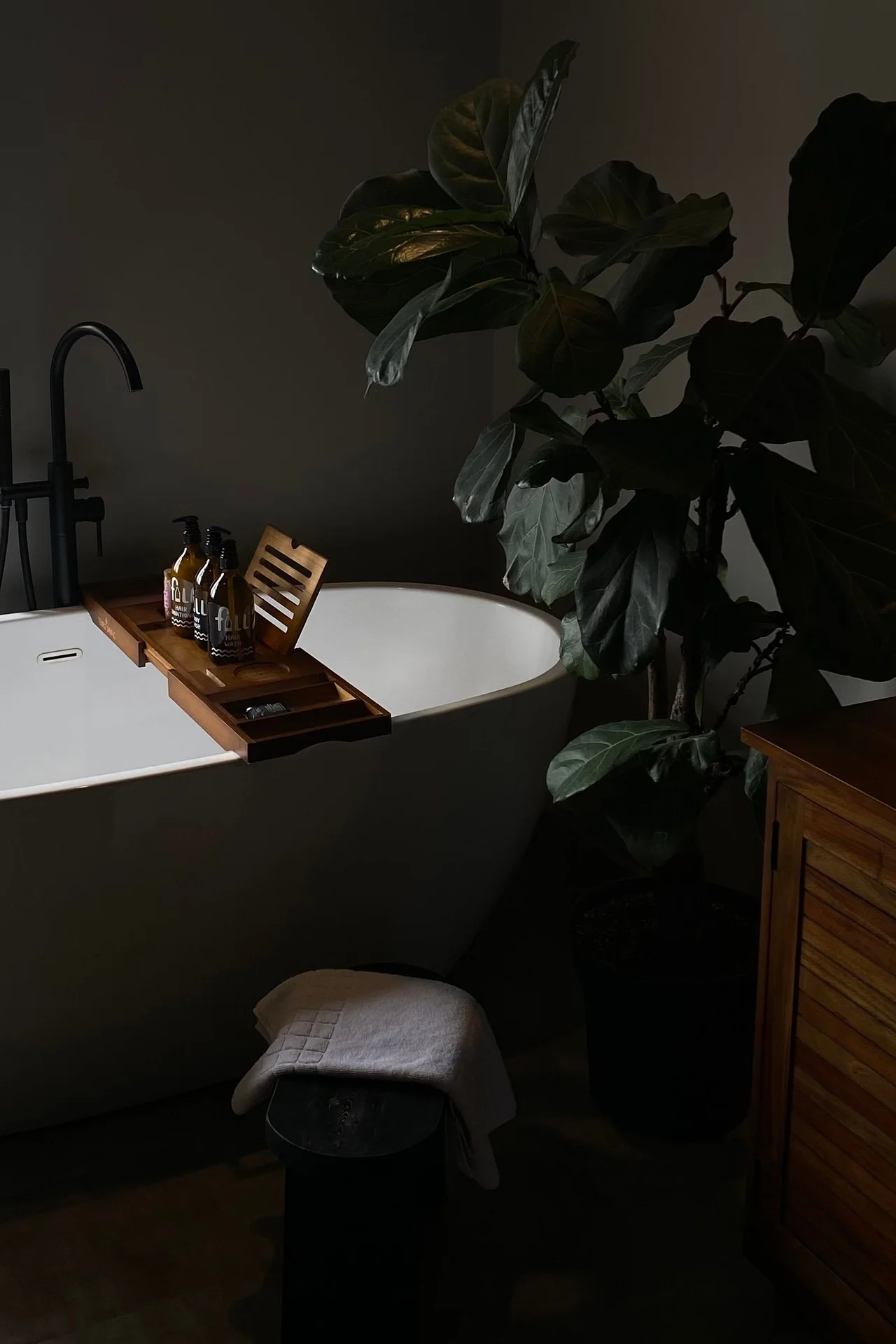 Small wooden stool beside a bathtub holding a towel and candle