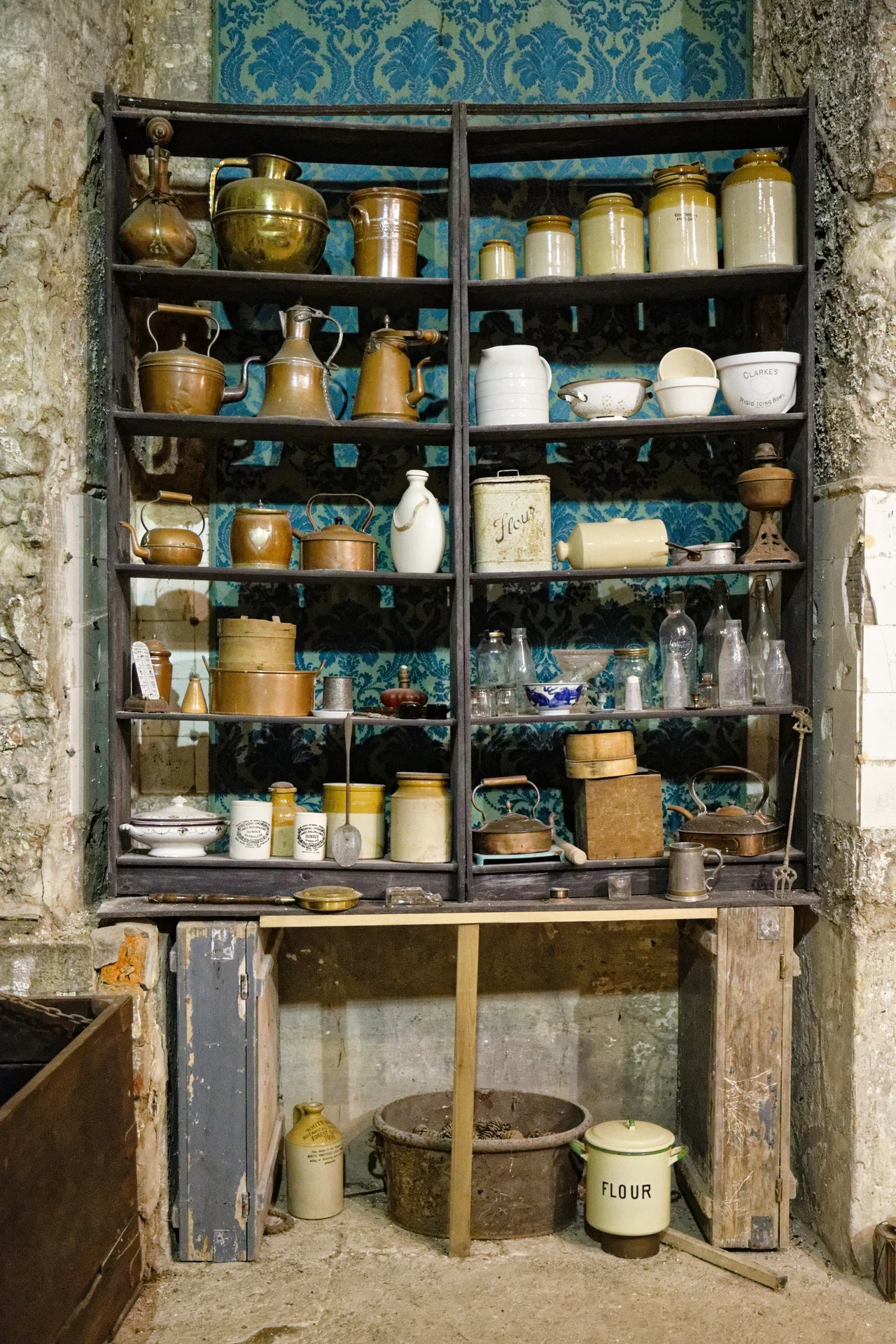 Open kitchen shelf holding white bowls plates and glass jars in a small apartment