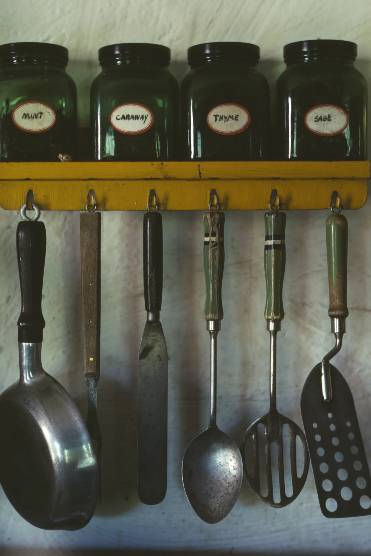 Pegboard wall in a small kitchen holding pots pans and cooking tools on hooks